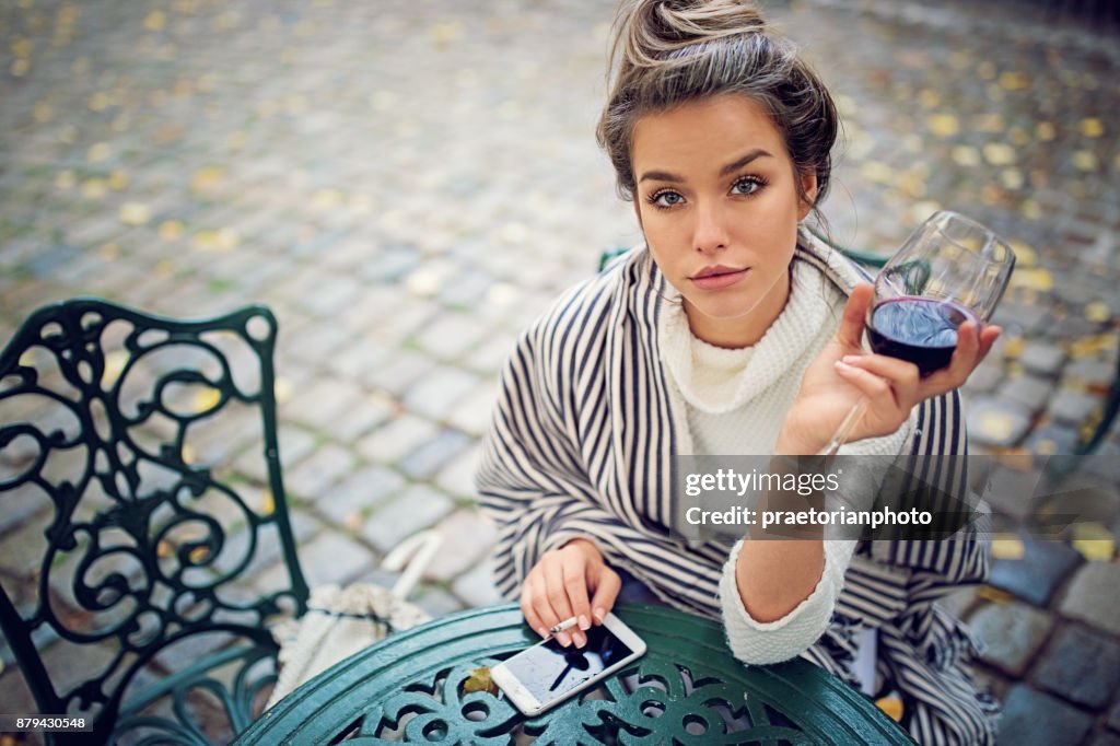 Depressed woman is drinking wine, smoking and holding her broken phone in a rainy day