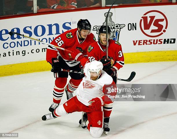 Kris Versteeg and Samuel Pahlsson of the Chicago Blackhawks knock down Kris Draper of the Detroit Red Wings during Game Three of the Western...