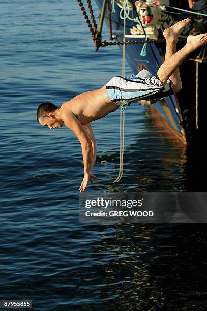 Man dives into the water to cool off in front of the bow of the three-masted barquentine sail training ship 'Leeuwin II' in the harbour of the...