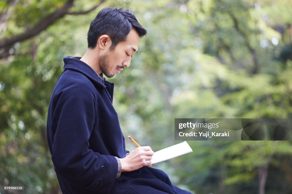 Young man sketching in the woods lit with sunshine