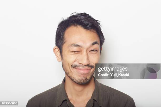 closeup face of young man with a beard winking - winking stock pictures, royalty-free photos & images