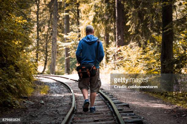 young man walking alone on railway track in autumn forest - camera bag stock pictures, royalty-free photos & images