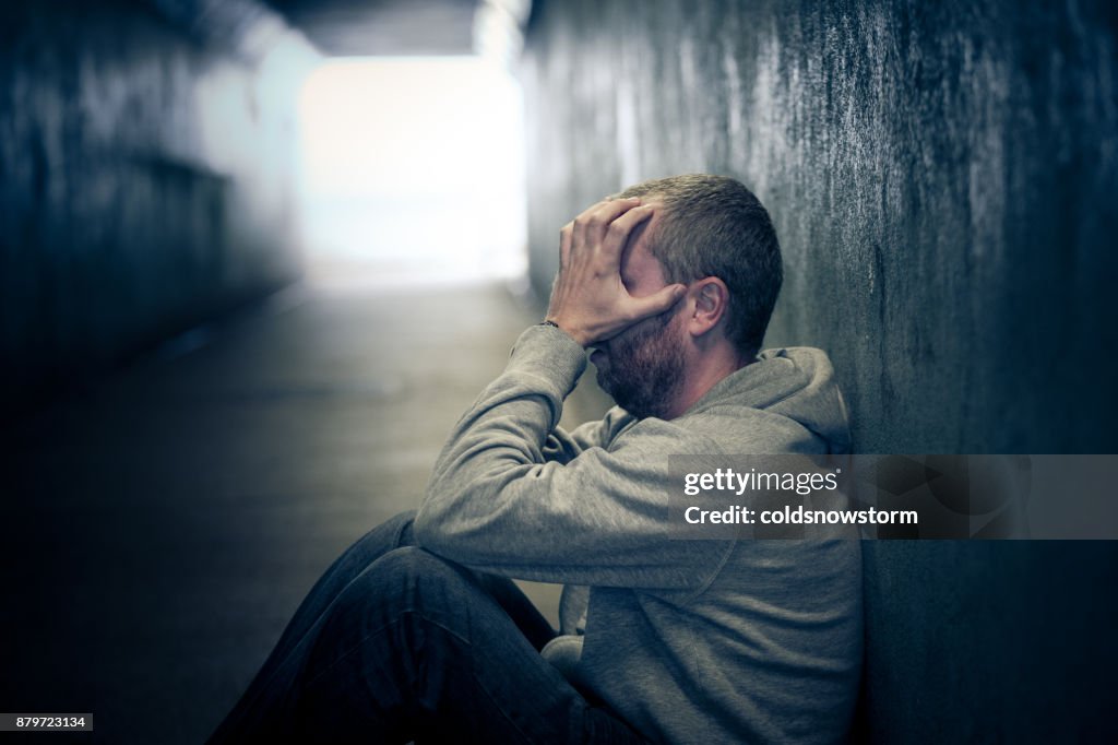 Jonge dakloze Kaukasisch mannetje zit in de metro van de donkere tunnel