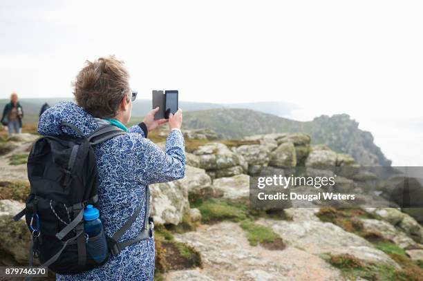 senior woman taking photo with phone on coastal hike. - vista trasera de tres cuartos fotografías e imágenes de stock