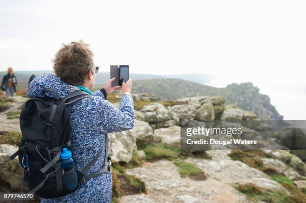 senior woman taking photo with phone on coastal hike. - vista traseira a três quartos - fotografias e filmes do acervo