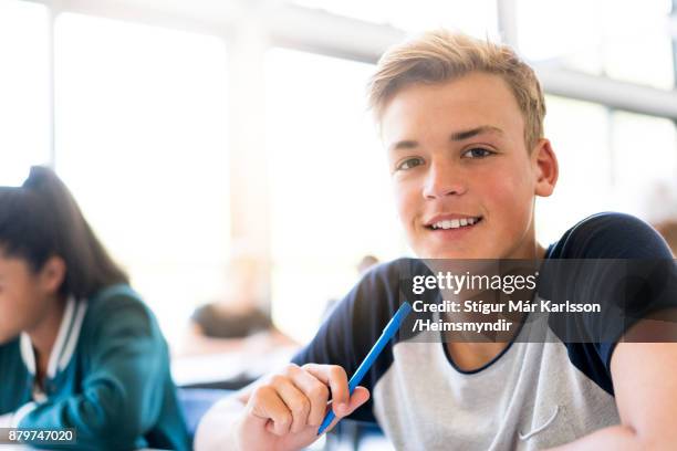 lächelnde männliche teenager-studentin im klassenzimmer sitzen - 14 15 stock-fotos und bilder