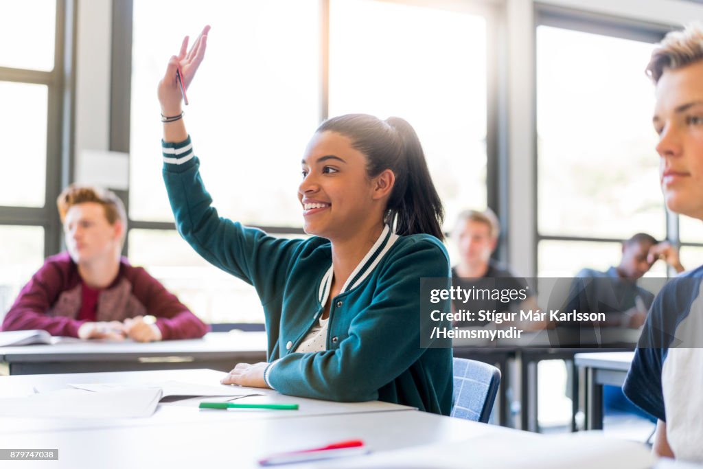 Lachende tiener student verhogen hand in klaslokaal