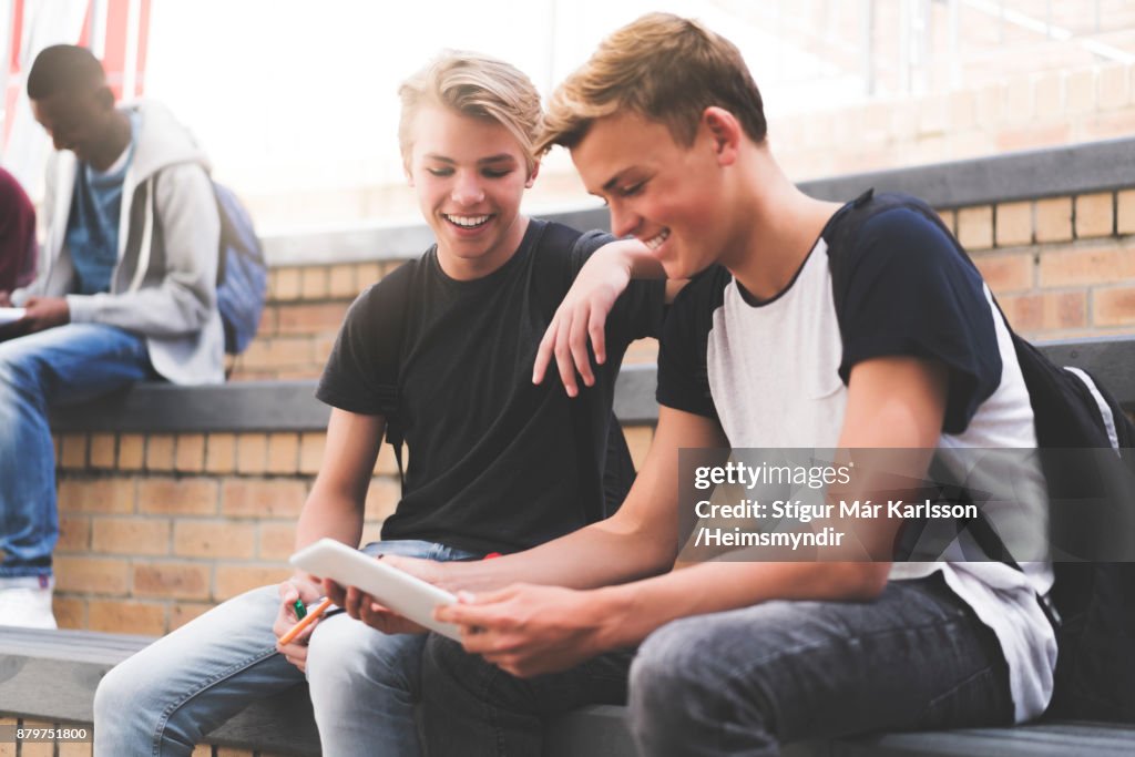 Happy high school teenage students sharing tablet