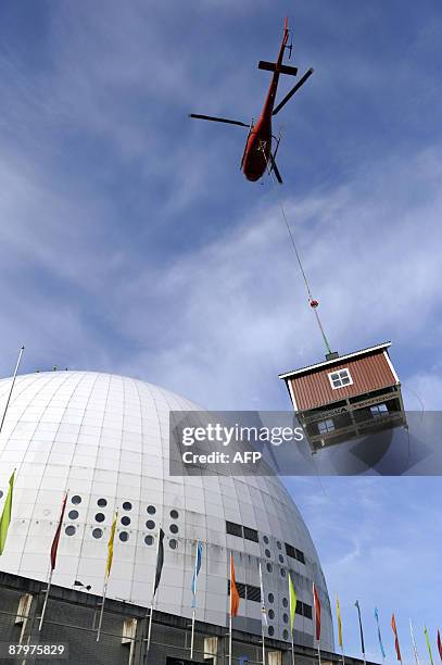 Helicopter places a red cottage, designed by Swedish artist Mikael Genberg, atop the Ericsson Globe Arena, where it will remain for the summer, on...