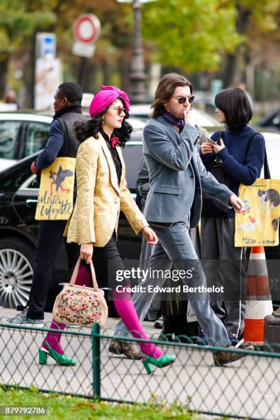 Guest wears a pink hat, sunglasses, a yellow blazer jacket, black skirt, pink tights, green shoes, a color bag, outside Margiela, during Paris...