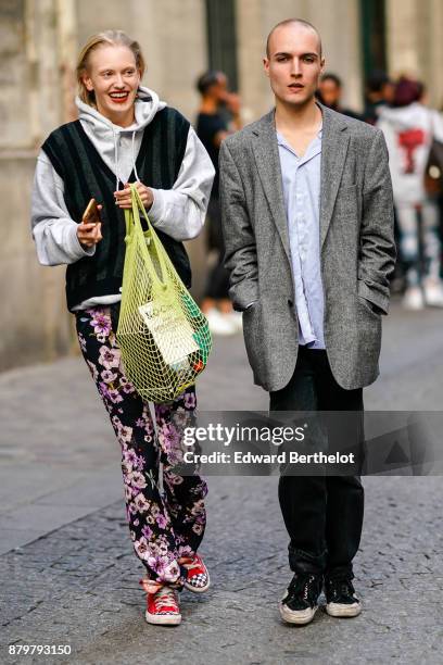 Guest wears a gray hoodie, a yellow fishnet bag, flower print pants, red shoes ; a guest wears a blazer jacket, a blue shirt, black pants, outside...