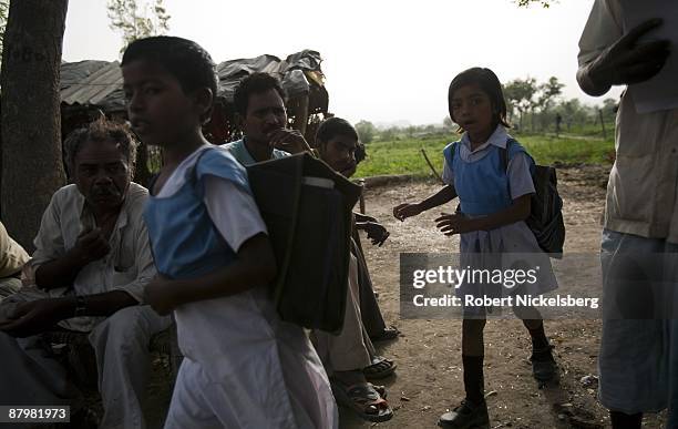 Residents living in a slum area sit as two girls walk to school near a newly dug roadway April 21, 2009 where agricultural areas they and members of...