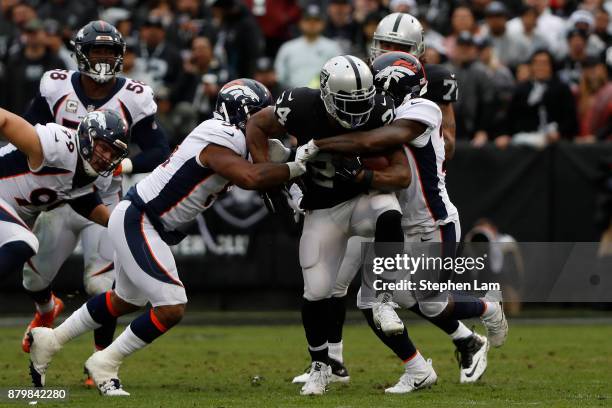 Marshawn Lynch of the Oakland Raiders drives the ball as he is being tackled by Todd Davis and Darian Stewart of the Denver Broncos during the first...