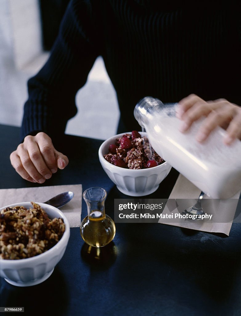 Person pouring milk on bowl of granola