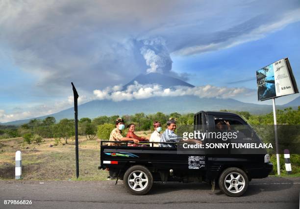Balinese people ride on an open car past Mount Agung erupting seen from Kubu sub-district in Karangasem Regency, on Indonesia's resort island of Bali...