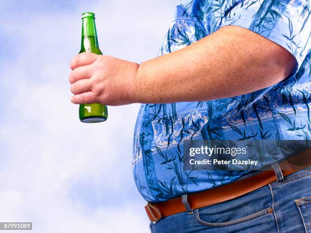 obese man holding beer bottle against sky. - barrigón fotografías e imágenes de stock