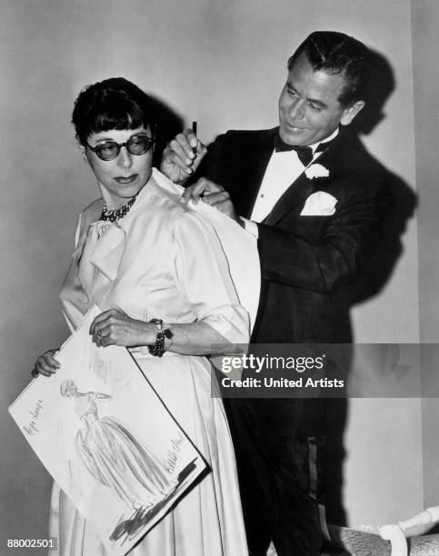 Canadian-born actor Glenn Ford autographs one of the sketches American costume designer Edith Head created for the film 'Pocketful Of Miracles', on...