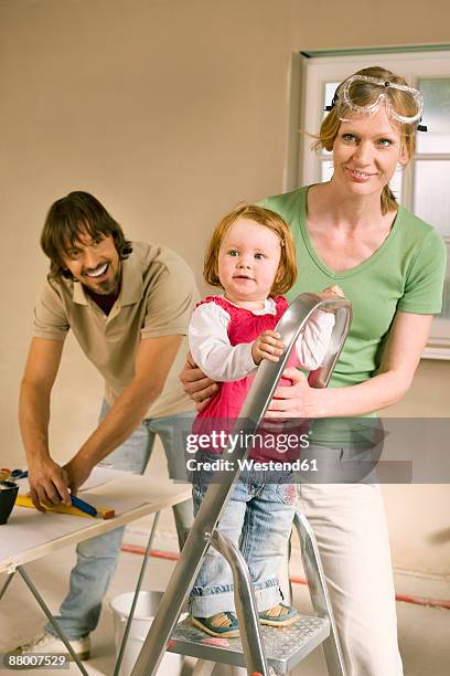 family, baby girl (1-2) on step ladder, man preparing wallpaper - bent ladder stock pictures, royalty-free photos & images