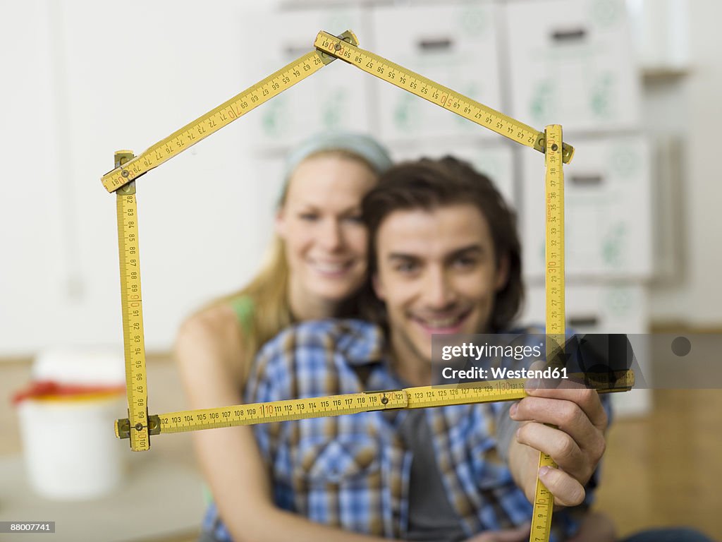Young couple making house shape with folding rule, portrait