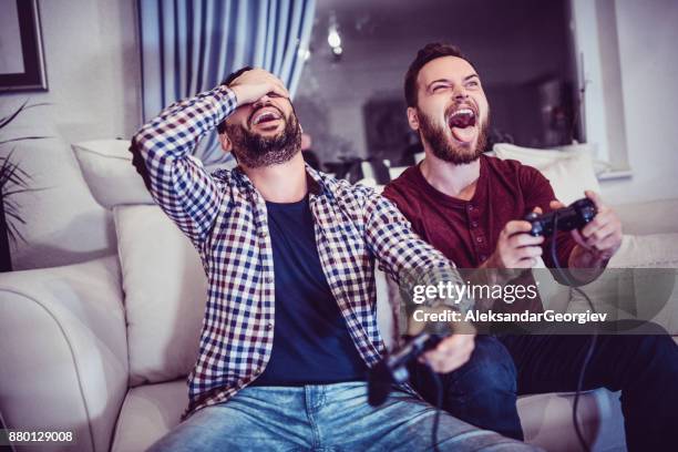 handsome man is defeating his older brother in video games - car racing game stock pictures, royalty-free photos & images