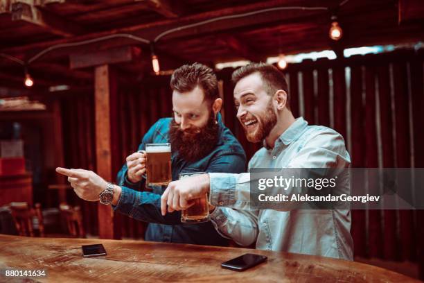 dos sonrientes amigos guapos mirando y apuntando a las chicas en un bar - locura fotografías e imágenes de stock