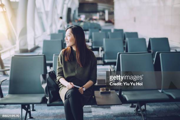 young asian woman holding passport and boarding pass on hand waiting in the departure lounge in airport - yiu yu hoi stockfoto's en -beelden