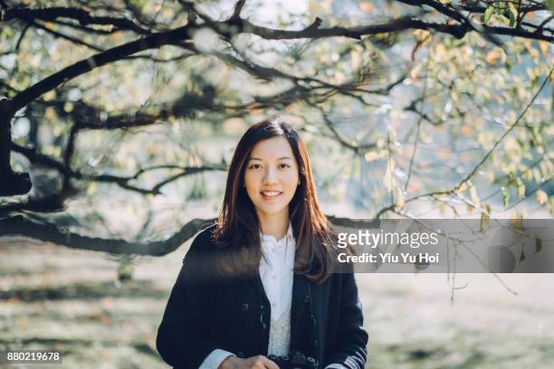 portrait of beautiful asian woman holding camera enjoying the sunlight and scenics in nature - yiu yu hoi stock pictures, royalty-free photos & images