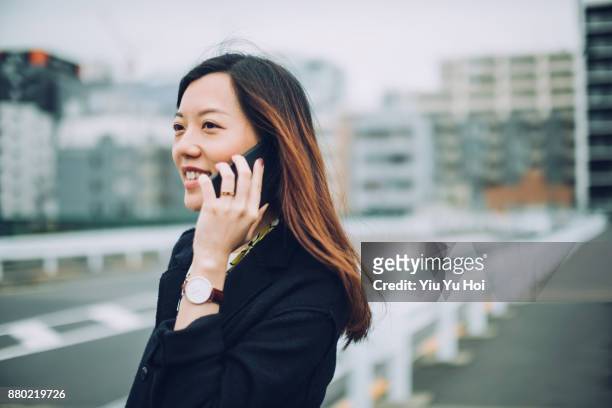 confident asian woman talking on smartphone outdoors with cityscape in background - yiu yu hoi stockfoto's en -beelden