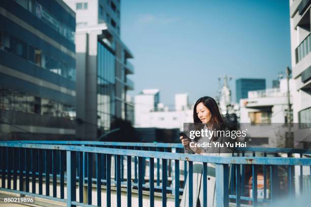 young businesswoman checking emails on mobile phone against urban cityscape - yiu yu hoi stockfoto's en -beelden