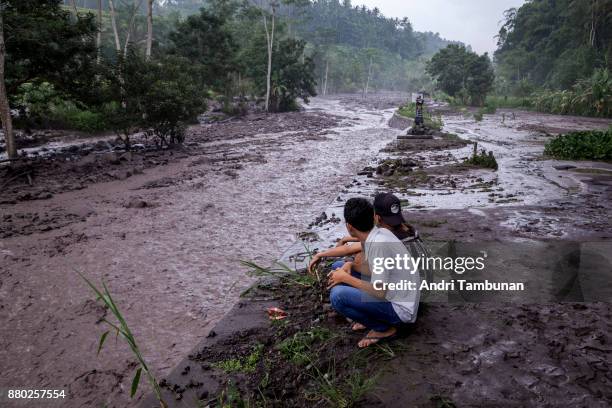 Volcanic material from Mount Agung flows through a local river in Gesing Village while villagers are seen watching nearby on November 27, 2017 in...