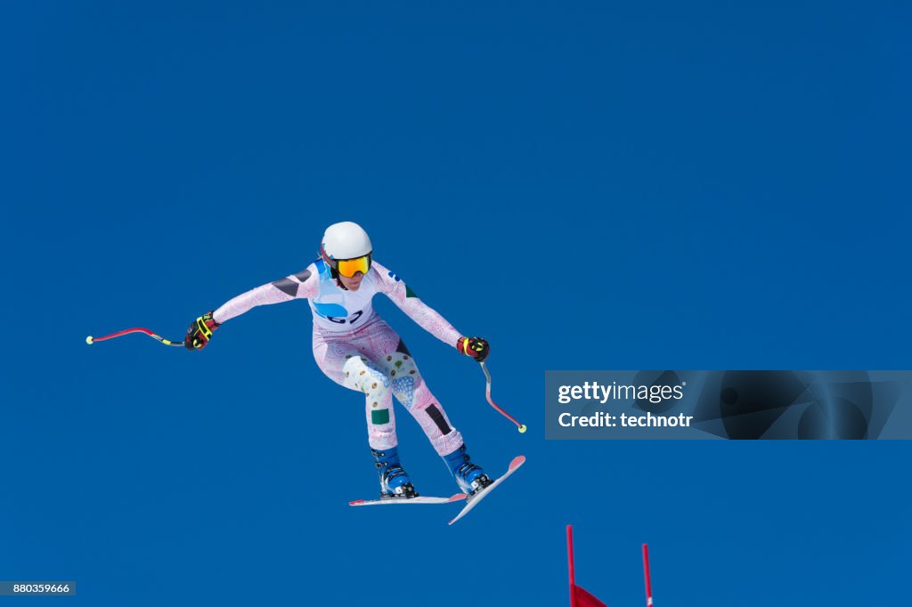 Professional female skier jumping on the red gate during downhill race