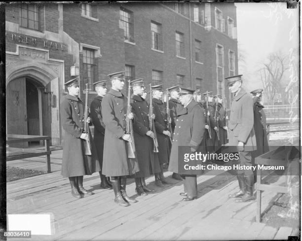 Full-length portrait of John Philip Sousa, American composer and bandmaster, standing in front of a group of young men wearing military uniforms and...