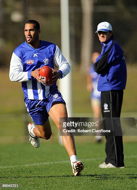 Josh Gibson of the Kangaroos runs upfield as coach Dean Laidley looks on during a North Melbourne Kangaroos AFL training session held at Arden Street...
