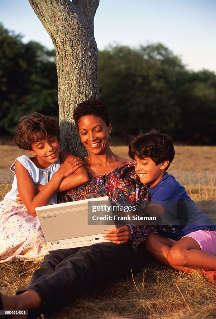 Mother and daughters (6-10) using laptop under tree