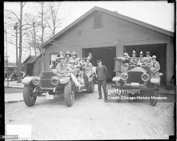 Full-length group portrait of a group of Girl Scouts sitting and standing on two large automobiles in front of a building at Great Lakes Naval...