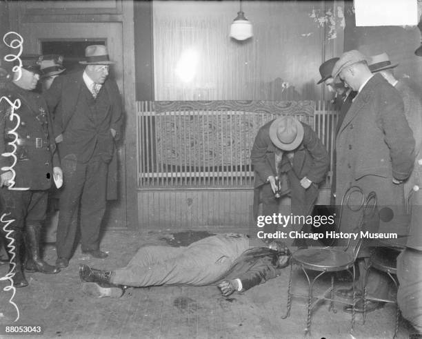 Image of the corpse of murder victim Ole Scully lying on the floor in a room in Chicago, Illinois, 1928. A policeman wearing a suit is leaning over...