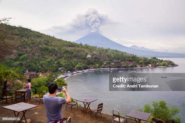 Tourist taking a photo of Mount Agung spewing volcanic ash from the popular Sunset Point in Amed on November 28, 2017 in Karangasem, Island of Bali,...