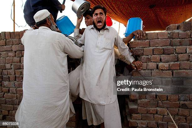 Kitchen guard yells as he pushes back a hostile crowd as Pakistani internally displaced push and shove to get food for dinner at the Chota Lahore...