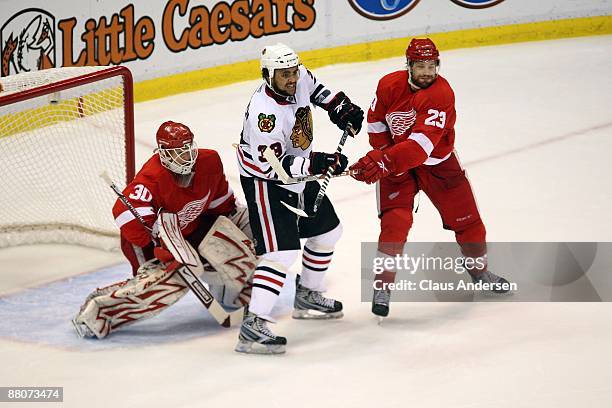 Dustin Byfuglien of the Chicago Blackhawks sets up on offense in front of the net between goalie Chris Osgood and Brad Stuart of the Detroit Red...