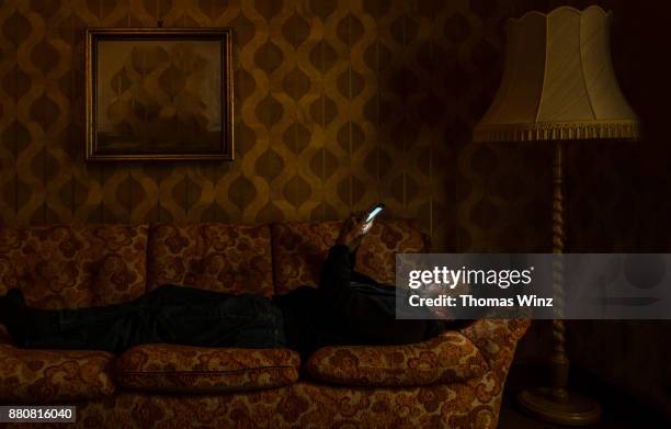 man looking at his cell phone on a couch - antique sofa styles foto e immagini stock