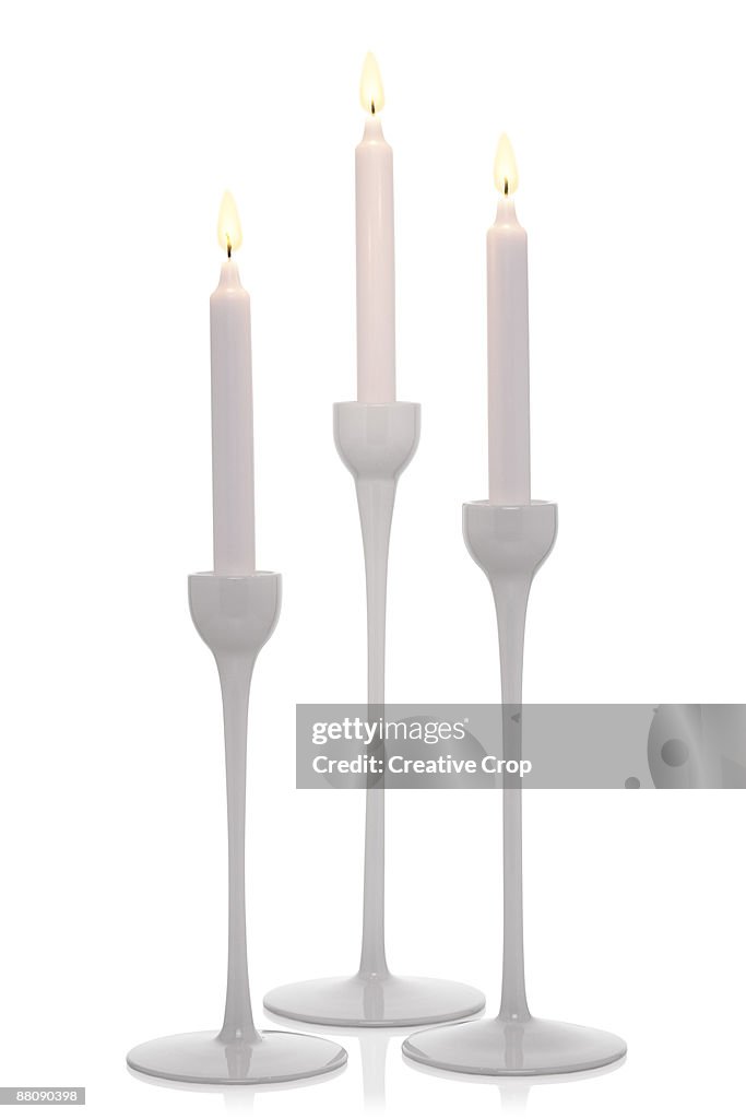 Three white candlesticks with light white candles