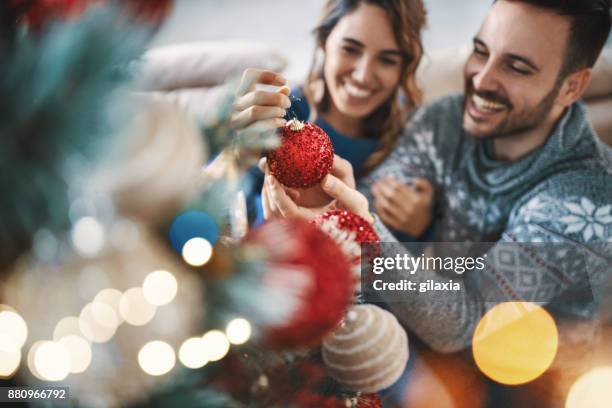 young couple decorating a christmas tree. - decorating christmas tree stock pictures, royalty-free photos & images