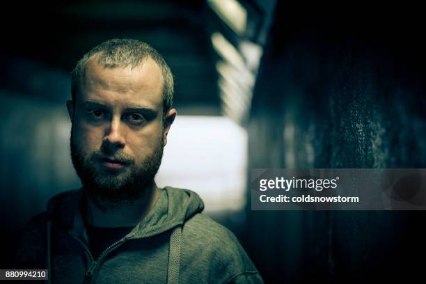 young homeless caucasian male standing and looking at camera in dark subway tunnel - psychiatric ward stock pictures, royalty-free photos & images