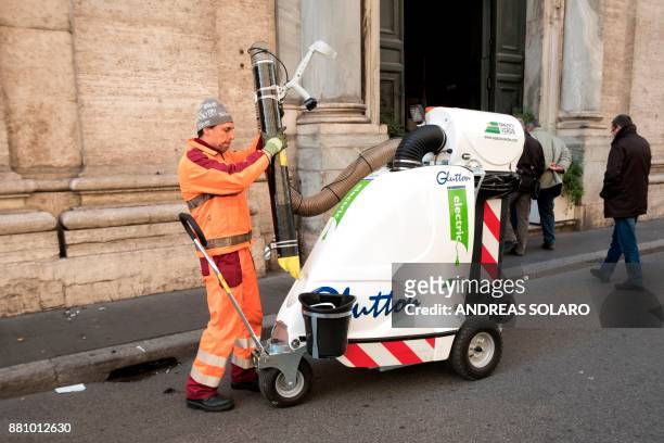 City cleaning worker of the Azienda Municipale Ambiente , uses an electric vacuum to clean a sidewalk on November 28, 2017 in central Rome. / AFP...