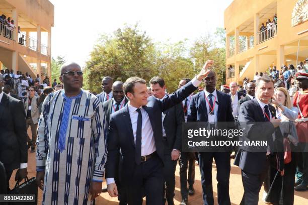 French President Emmanuel Macron salutes residents, walking with Burkina Faso's President Roch Marc Christian Kabore , as he leaves the Ouagadougou...