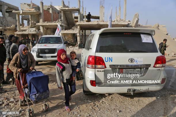 Syrians walk past vehcicles of the International Committee of the Red Cross and the United Nations during a humanitarian delivery in the al-Nashabia...