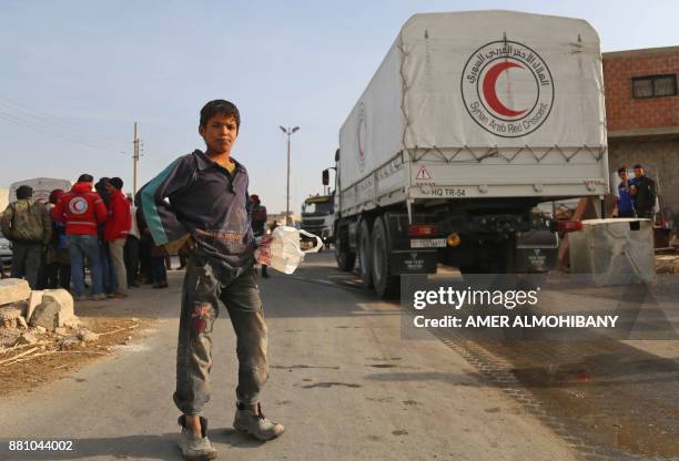 Syrian child stands next to vehcicles of the International Committee of the Red Cross during a humanitarian delivery in the al-Nashabia town, in the...