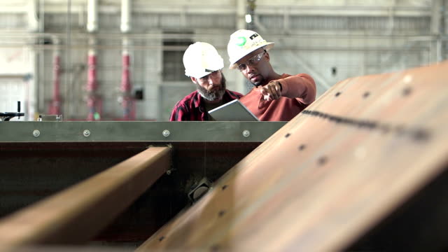 Two workers wearing hardhats, looking digital tablet