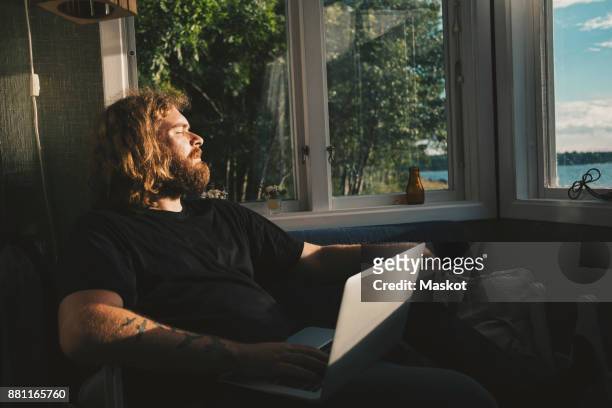 man holding laptop while resting by window at holiday villa - holiday house stock pictures, royalty-free photos & images