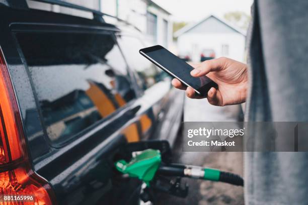 man using mobile phone while refueling car at gas station - car parked stock pictures, royalty-free photos & images